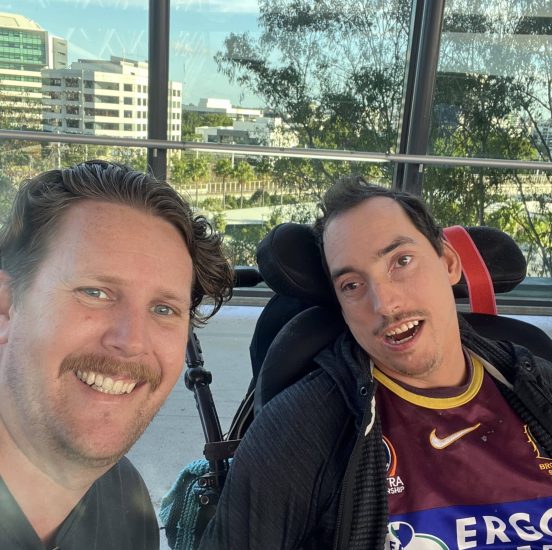 Two men one in wheelchair at a sports game smiling